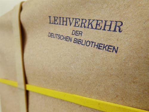 Foto: Nahaufnahme eine Pakets in braunem Packpapier und gelbem Band mit einem Stempelaufdruck: Leihverkehr der deutschen Bibliotheken. 